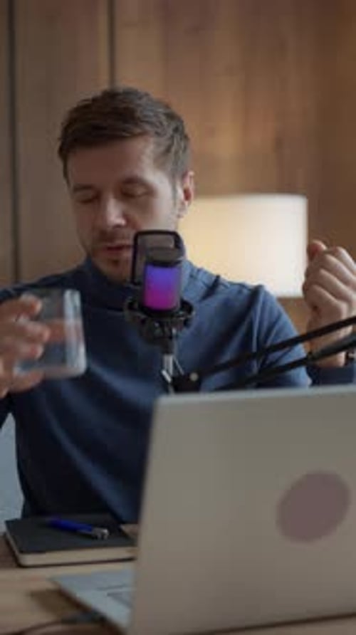 Man Drinking Water During Podcast Recording at Laptop in Home Office