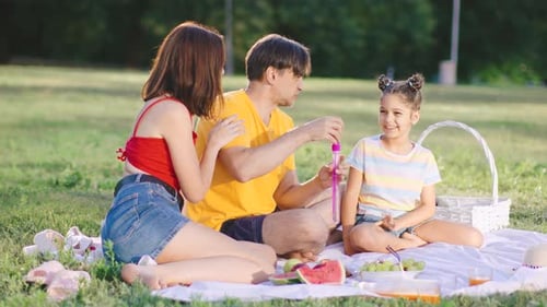 Family Enjoys a Summer Picnic with Bubbles and Fresh Fruits in a Sunny Park Setting