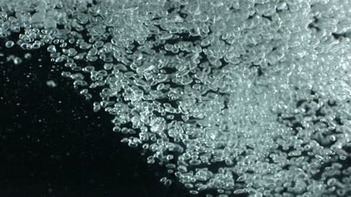 Winzige Wasserblasen steigen in Zeitlupe vor einem dunklen abstrakten Hintergrund auf
