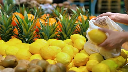 Mujer recogiendo limones en una bolsa reutilizable en una tienda. Temáticas del Día de la Tierra y la Ecología