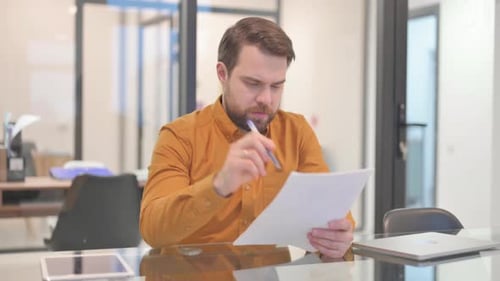 Focused Man Reviews Documents at Modern Office Desk