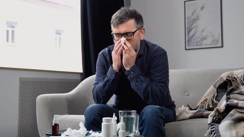 Man Sick with Cold Blowing Nose on Couch