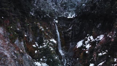 Eine ruhige Luftaufnahme eines winterlichen Bergwaldes mit einem Wasserfall, der durch die Landschaft fließt in