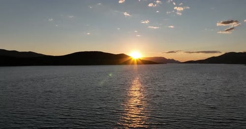 A serene sunset scene unfolds over a tranquil body of water. The sun dips below the horizon, casting