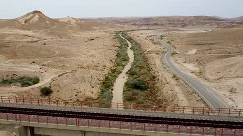 aerial forward slow drone shot of a dry stream below a bridge with a view of the desert and an empty