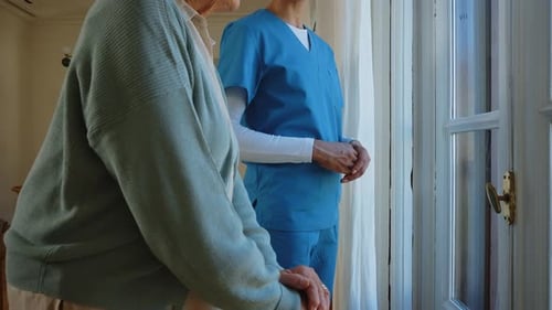 Senior woman with home caregiver at window