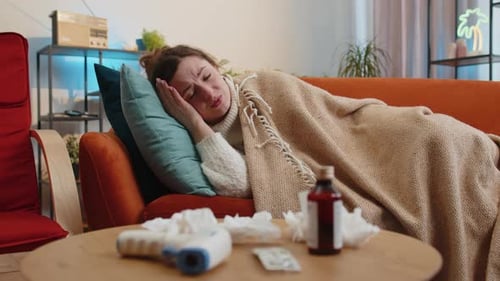 Une femme malade souffrant de rhume ou d'allergie, assise sur le canapé de la maison, éternuant, essuie de la morve dans une serviette