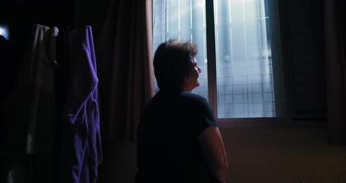Adult Looking Out Window in Dark Room