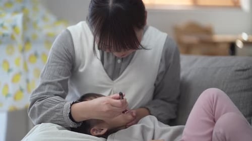 Woman Cleaning Child's Face on Sofa at Home