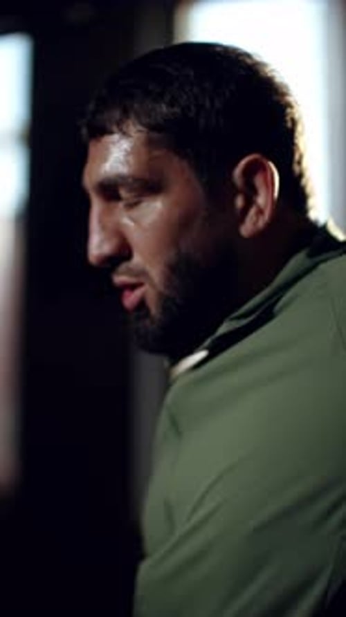 Bärtiger Boxer dehnt die Schultern und wärmt die Nackenmuskulatur vor dem harten Training im dunklen Fitnessstudio mit