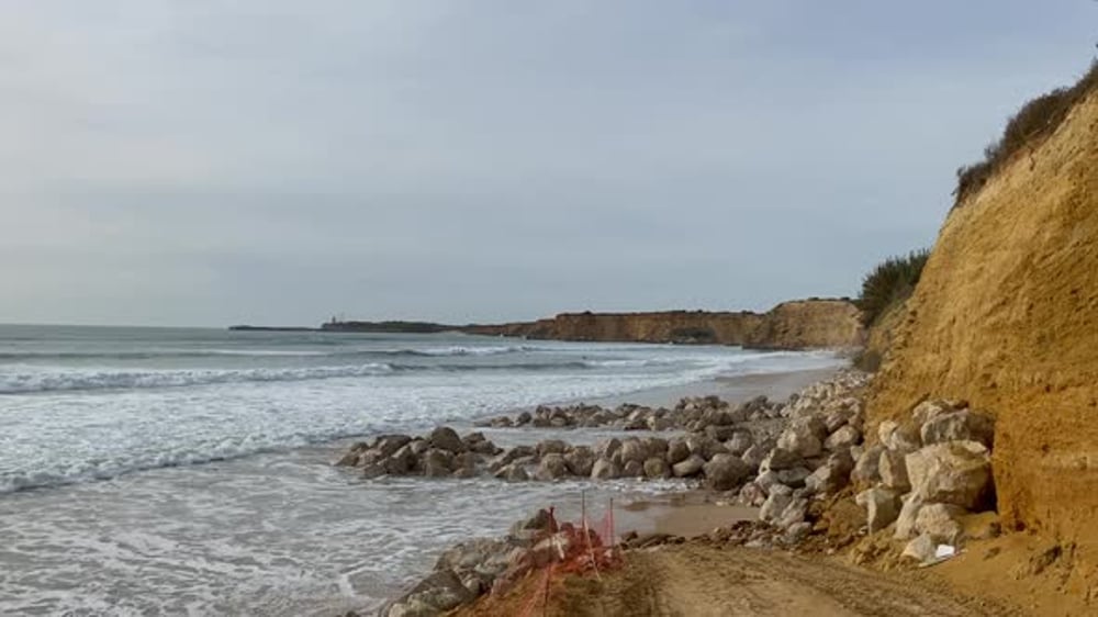 Sea defences of piled rocks protect the eroding cliffs while waves push ...