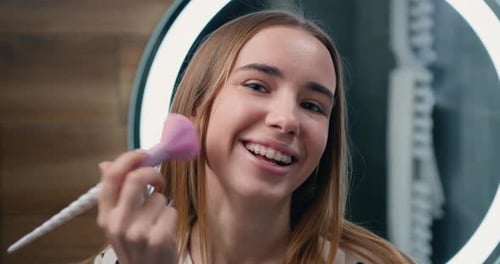Maquillaje facial. Primer plano de una hermosa joven poniendo rubor con un cepillo cosmético en el baño