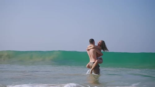 Fit Man Carrying Woman in Sea Surf Waves Water Makes Splashes Happy Couple in Love Having Fun in the