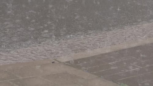 Zeitlupe von Regentropfen, die in Pfützen auf einem Bürgersteig und einer Straße plätschern und Wellen und ein Reflex erzeugen