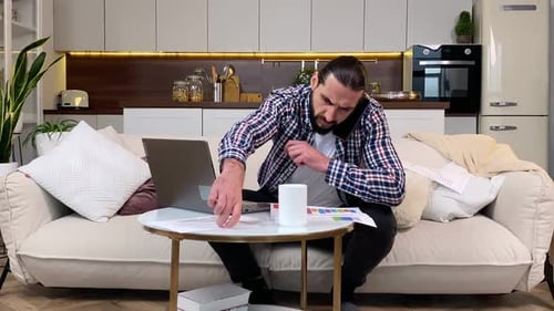 Man Working From Home on Laptop, Talking on Phone