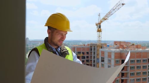 Close Up of Handsome Young Professional Male Constructor in Helmet Looking at Plan Draft at High