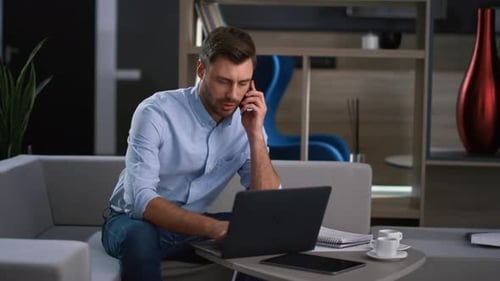 Man Working on Laptop and Talking on Phone
