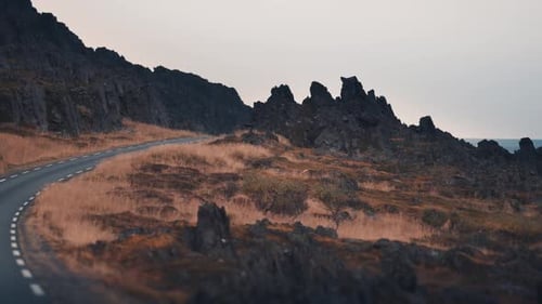 Dashcam view. Driving on the narrow asphalt road through the dark rocky landscape.