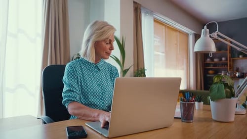 Happy mature businesswoman using laptop and working remotely from home