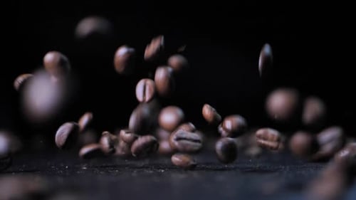 Braune Kaffeebohnen tanzen auf einem Tablett. Schwarzer Hintergrund verschwommen. Das Tablett dreht sich. Selektiver Fokus
