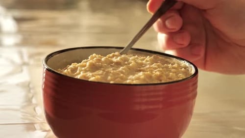 Oatmeal. Man stirring hot oatmeal in cup in sunny morning room