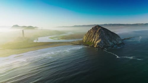 Magical sight of Morro Bay covered with thick fog. Triangle rock at the shore of Central coast