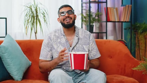 Bearded Man Eating Popcorn on Orange Couch