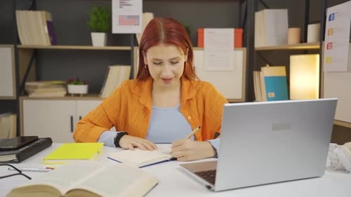 Woman Writing in Notebook at Desk with Laptop