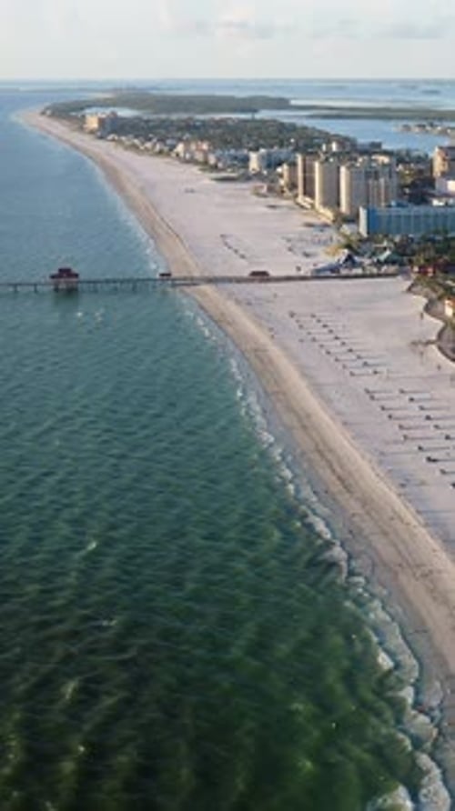Pier stretching into turquoise waters along wide sandy coastline with beachfront hotels