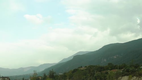 A car journey, a view from the window of mountains covered with trees and clouds above them.