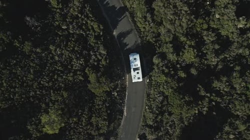 Bird's eye view of white camper van travelling along narrow winding road