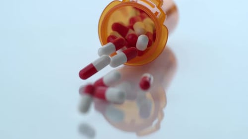 Pills spilling from prescription bottle onto reflective surface