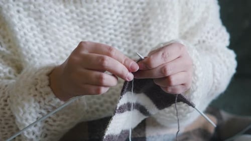 Weibliche kaukasische Hände stricken braunen Wollschal mit Stricknadeln