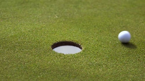 Ein Golfball, der das Loch verfehlt und dann in das Loch geschlagen wird.