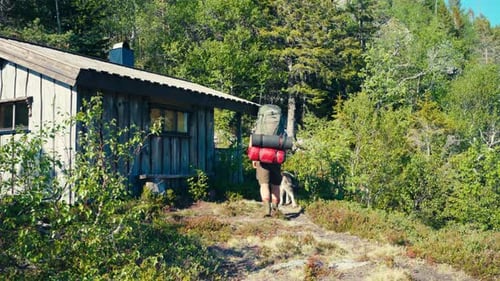 A Man and His Dog Walk Towards a Wooden Cabin on their Route From Seterdjupna to Malitjønna in Indre