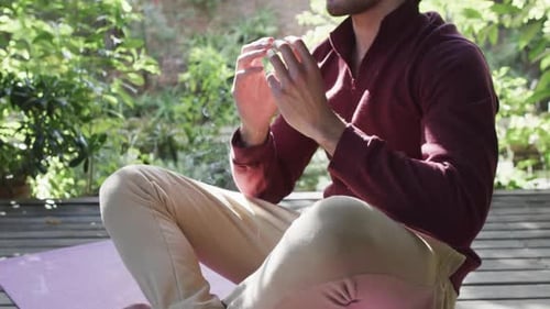 Midsection of caucasian man practicing yoga meditation on terrace in sunny nature, slow motion