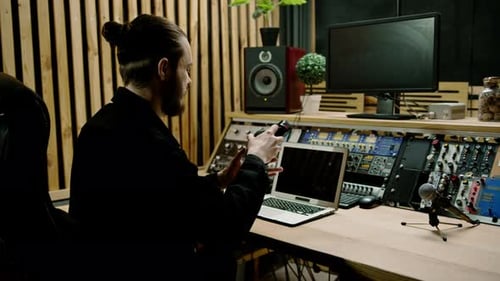 young sound engineer putting on headphones working in a professional music studio with monitors