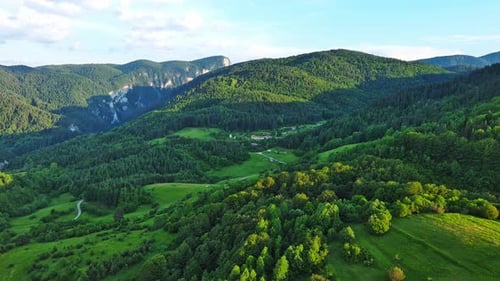 A Road Passes Hills Covered with Spruce Forests and Meadows Against a Cloudy Sky