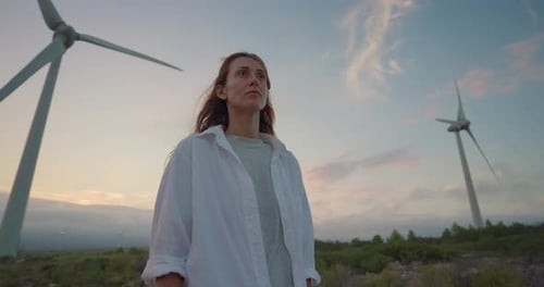 Una mujer con el pelo largo y rizado en el contexto de los molinos de viento que generan electricidad renovable Un