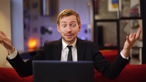 Frustrierter junger Mann im Anzug sitzt mit PC-Laptop auf der Couch und schreit.