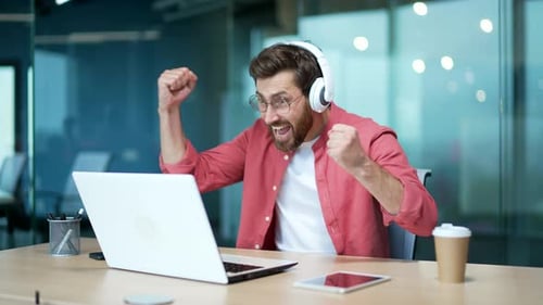 Excited Man Celebrates Success at Workplace Using Laptop