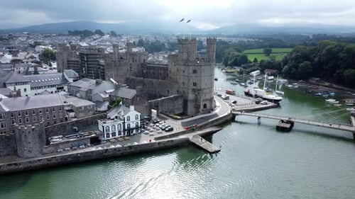 Ancient Caernarfon castle Welsh harbour town aerial view medieval waterfront landmark pull away reve
