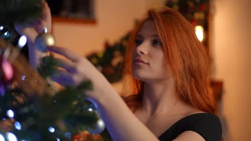 Woman Decorating Christmas Tree with Ornaments at Home
