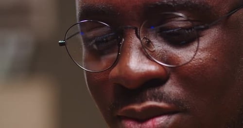 Close Up of Guy Face in Glasses with Laptop Screen Reflection at Home in Evening Young Afro American