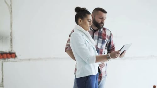 Joven pareja con tableta hablando y comprobando el proyecto en su nueva casa analizando