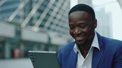 Portrait of African American Businessman Smiles Looking at Tablet on Street