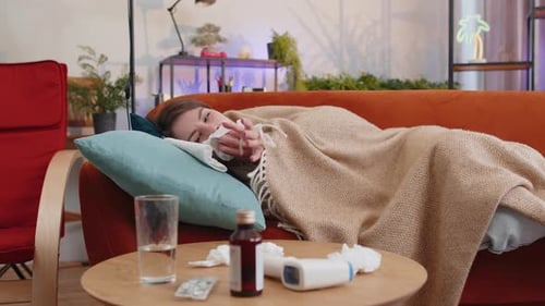 Une femme malade souffrant de rhume ou d'allergie, assise sur le canapé de la maison, éternuant, essuie de la morve dans une serviette