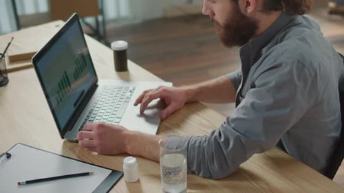 Man Massaging Wrists at Desk with Laptop