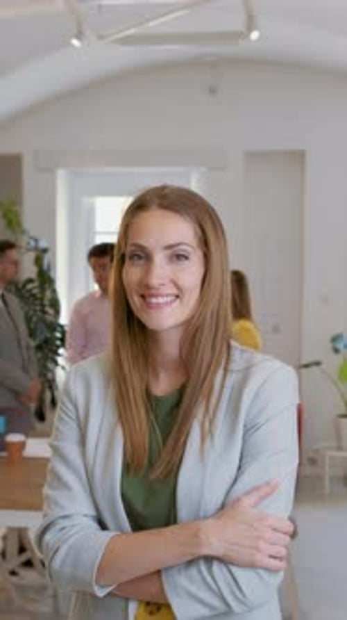 Portrait of smiling businesswoman in office with her colleagues in background.