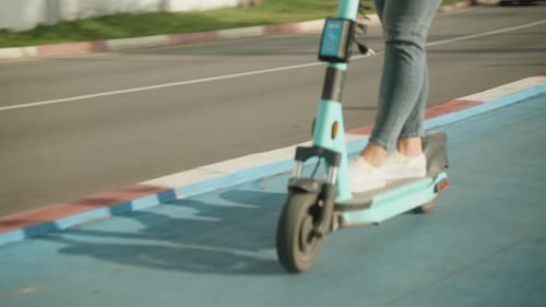 Jambes d'une jeune femme qui fait du scooter dans le parc.